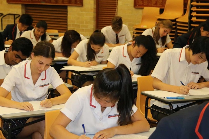 Students sit at exam tables, writing in exam papers