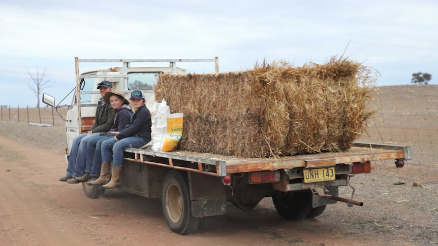 Scott family sitting on the back of a ute with hay also on it