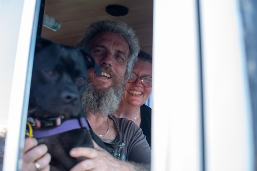A man and a woman, with a dog, in the front seat of their customised van.