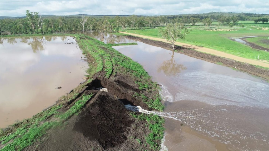 Water spills onto farmland from hole in irrigation dam wall.