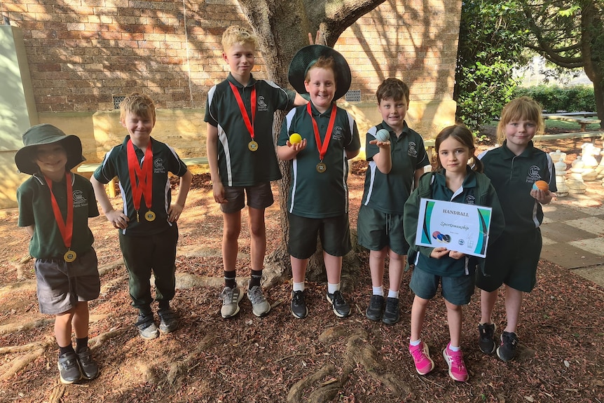 Small group of primary school students in green uniform hold medals and certificates