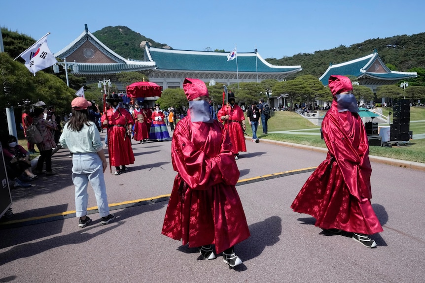 South Korean women dressed in traditional red royal robes, hat and face mask