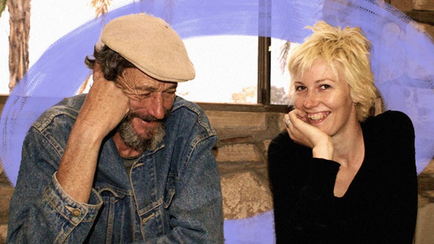 A man smiles while looking down. A young woman sits next to him smiling towards the camera.