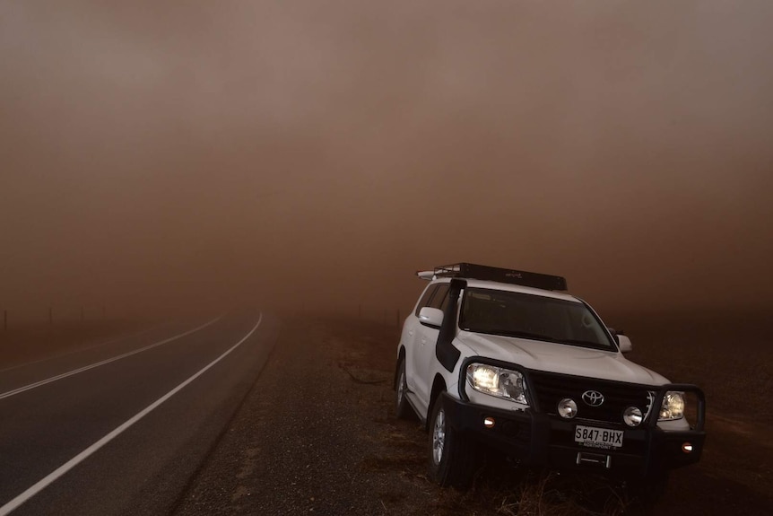 White 4WD in front of massive wall of dust