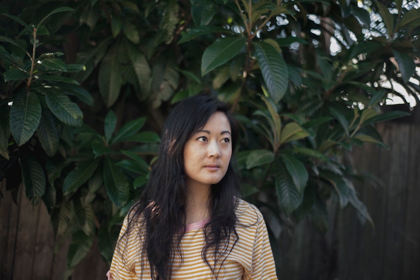 The novelist Jessie Tu standing in front of a plant out in the sunshine
