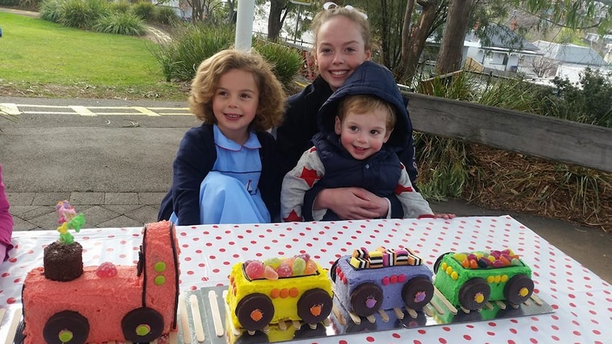 Mum and two young kids with a cake in the shape of a train