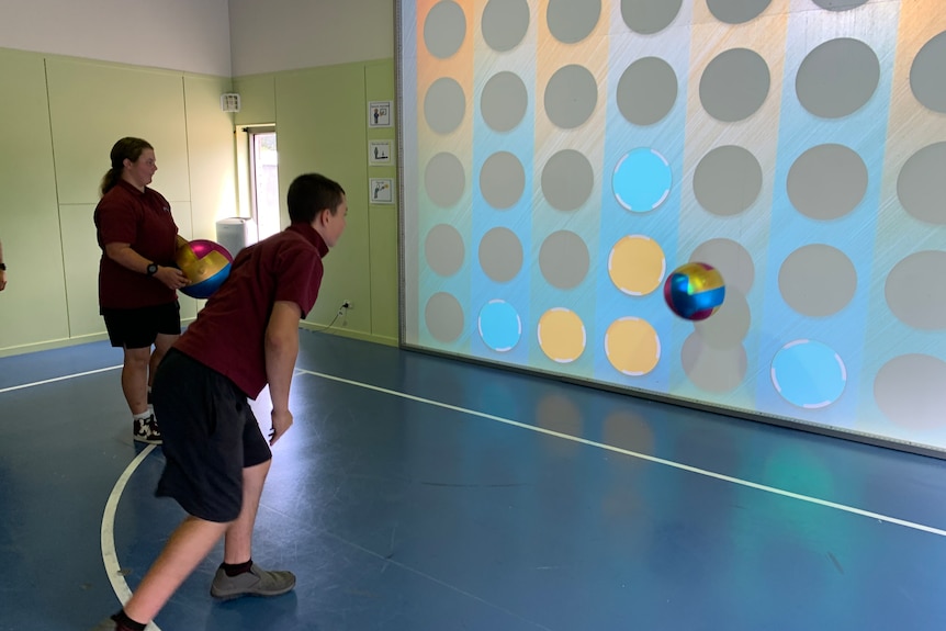Two students throw balls at a large, interactive screen covered with coloured dots