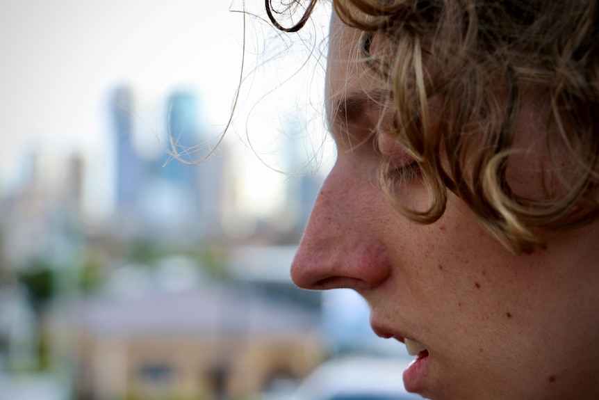 a young person closes their eyes, with a cityscape behind them