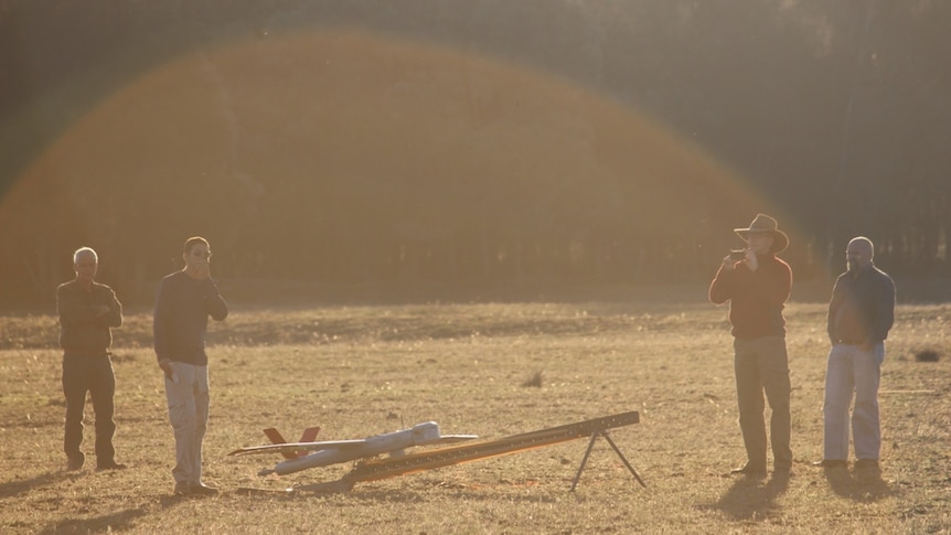 A military grade drone in a paddock in southern Queensland with four bystanders in the sunlight.
