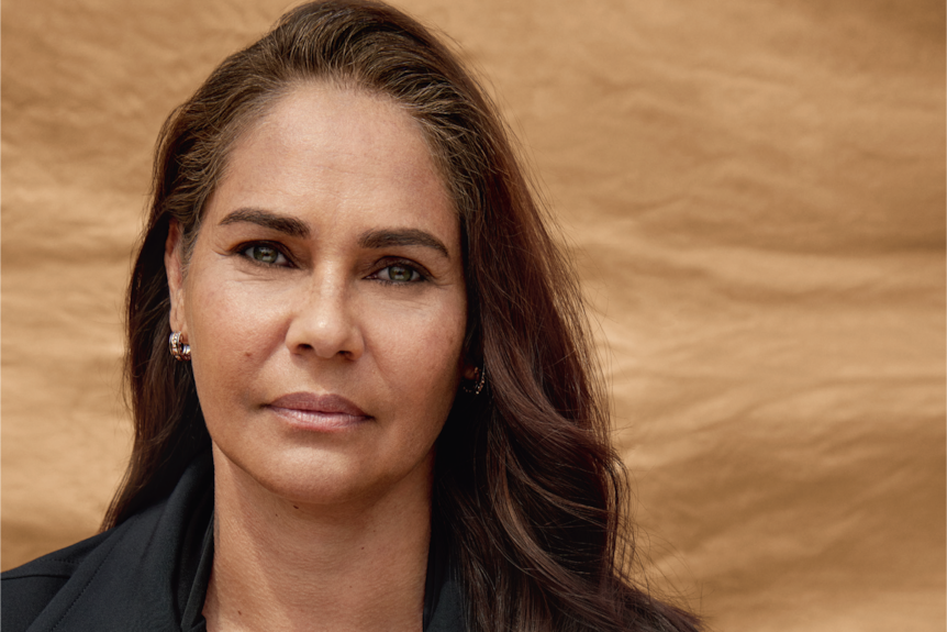 A woman with brown hair and green eyes in a black jacket with an Indigenous heart brooch