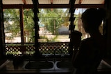 Silhouette of a woman standing at kitchen sink and looking out of louvre windows to palm trees