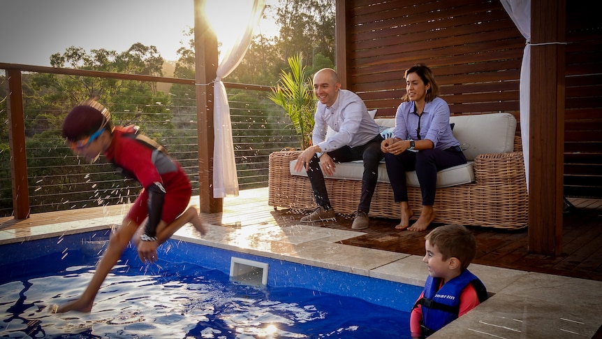 A young boy jumps into a pool while his parents watch on.