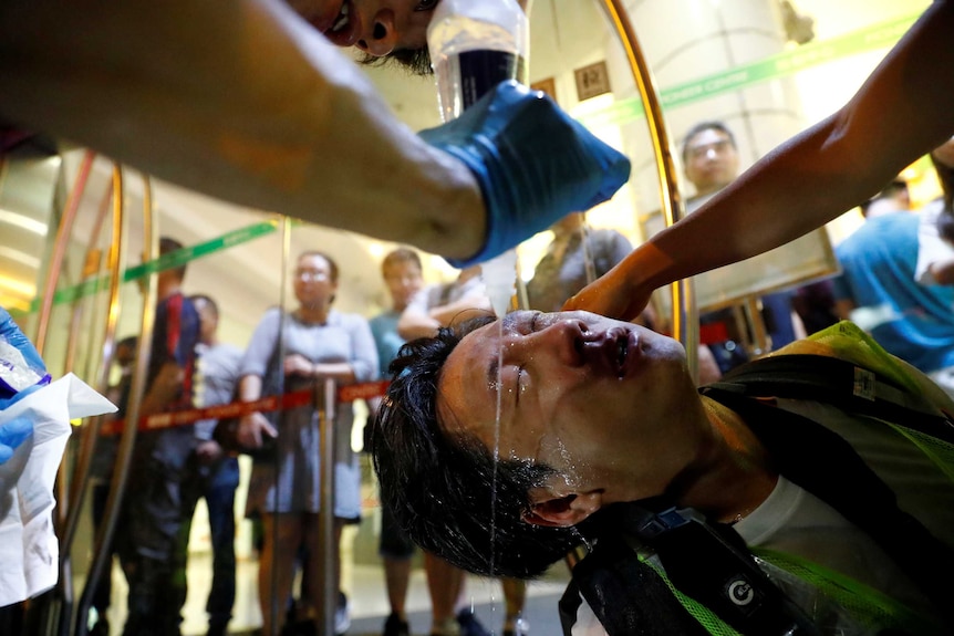 A close up photo shows a man getting treated for tear gas exposure, as a man sprays clear liquid over his eyes.