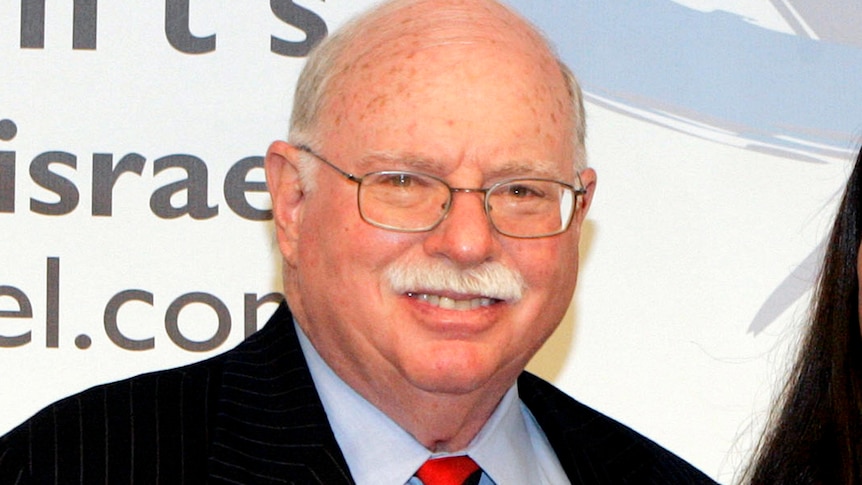 An older white man with glasses smiles for the camera.