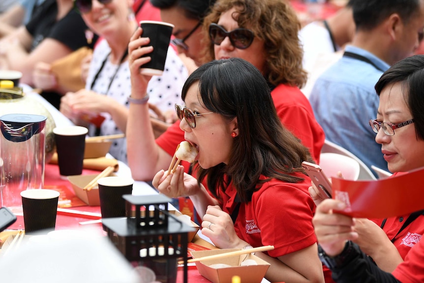 A woman eats a yum cha at a long table during Chinese New Year celebrations.