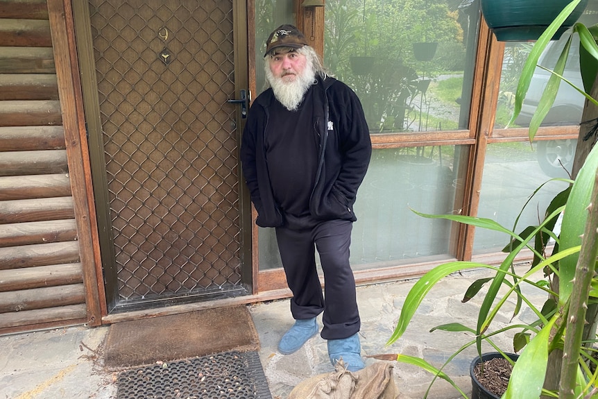 A man with a grey beard wearing a cap, a tracksuit and ugg boots outside a house