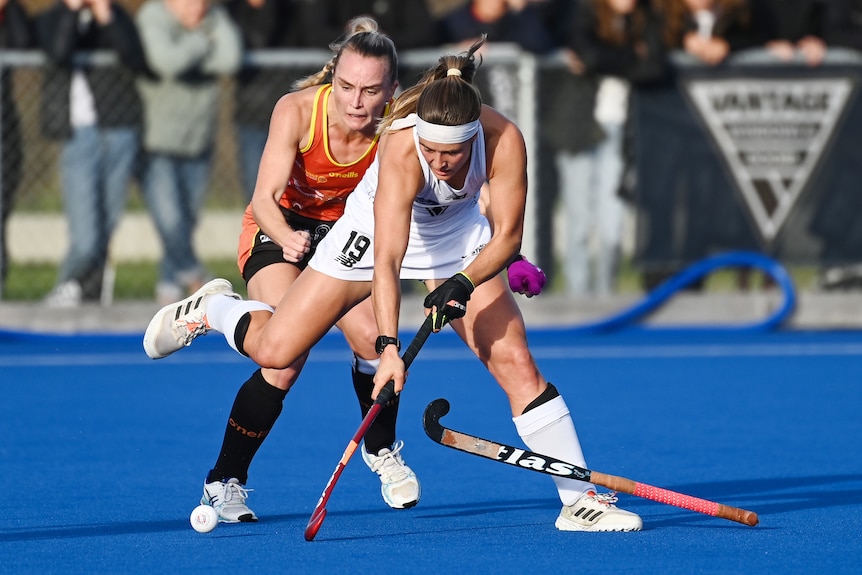 A New Zealand female hockey player tries to control the ball while under pressure from an Australian opponent.