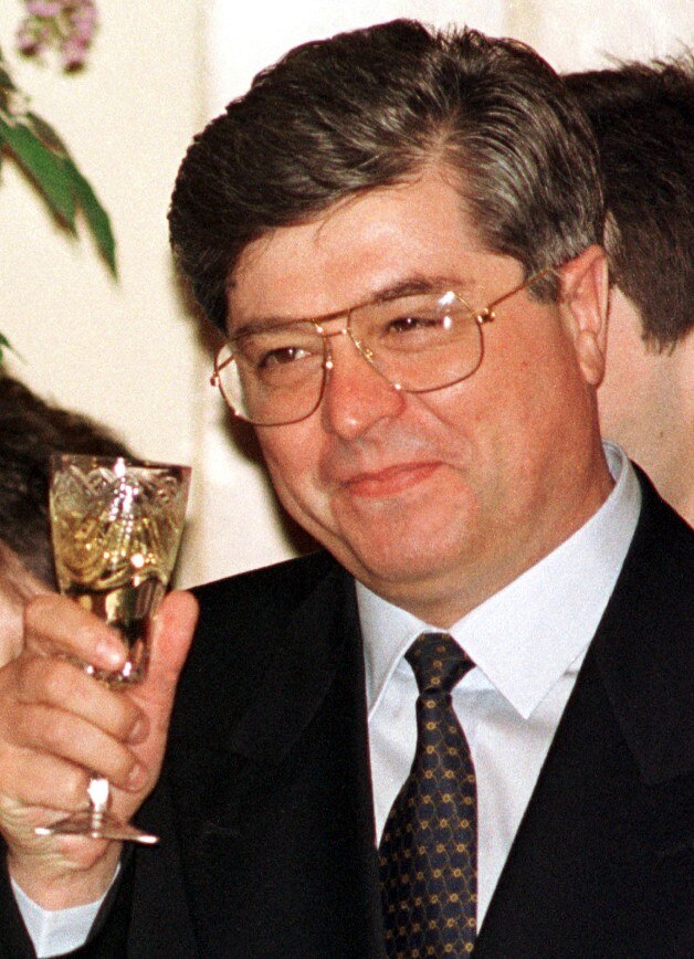 Un hombre con traje sostiene un vaso de líquido en la mano y tintinea vasos.