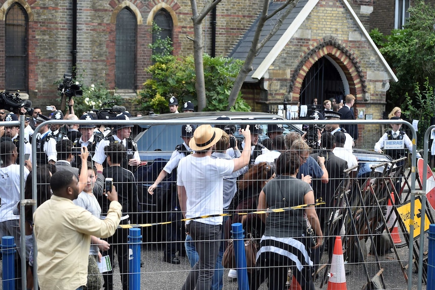 Police officers protect Theresa May from a crowd of people after she visited a church following the Grenfell Tower block fire