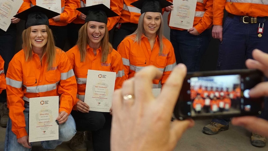 Four women wearing hi-vis and graduation hats pose for photo.