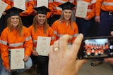 Four women wearing hi-vis and graduation hats pose for photo.
