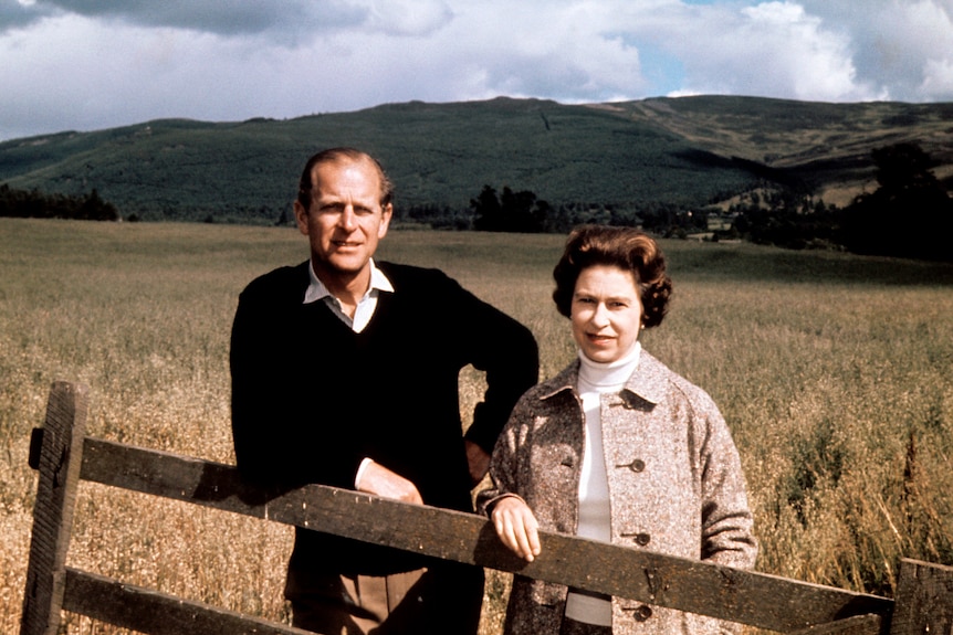 A man and a woman stand at a fence in the Scottish countryside.