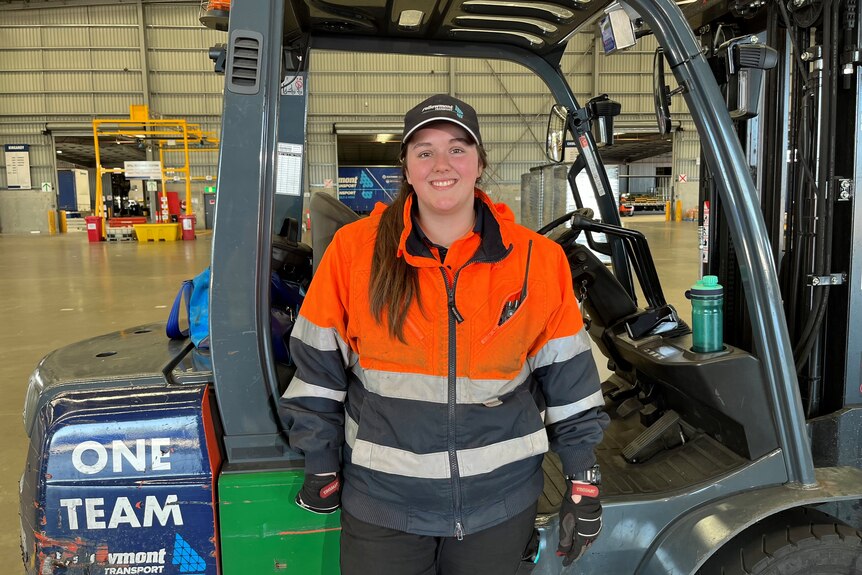 Younger truck driver Jade Harney with forklift behind her