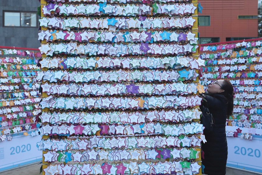 A woman hangs a paper note bearing her New Year wishes to a wire covered in other notes.