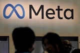 Meta logo in background in focus with blurry silhouette heads in foreground.