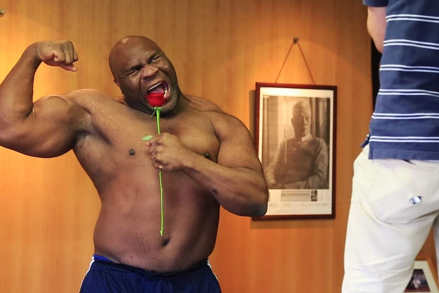 Bob Sapp flexes his muscles while holding a rose in a photo shoot.