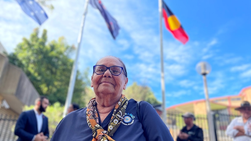 woman looks down at camera, aboriginal flag flies in the background