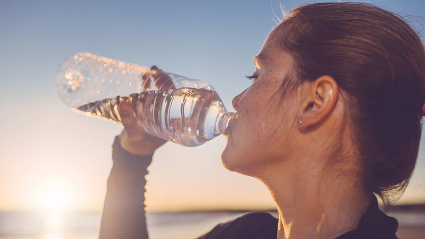 A woman drinking from a clear water bottle
