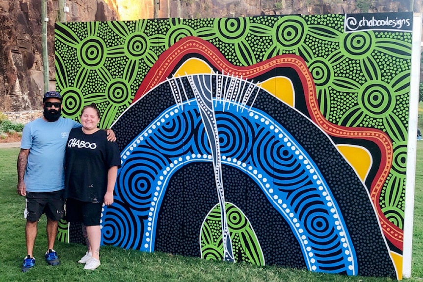 Two people standing by their Indigenous artwork
