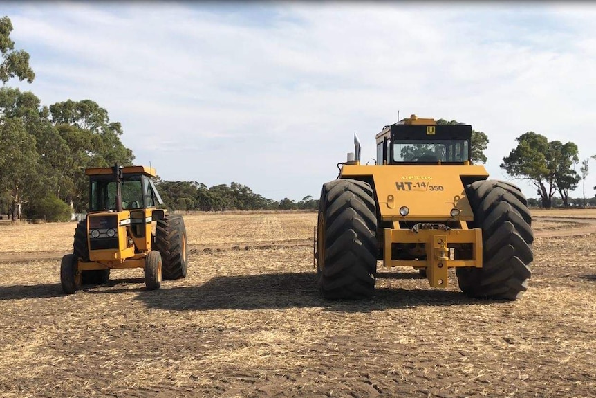 A small two-wheel-drive yellow tractor next to the Upton HT14-350, which looks four times bigger.