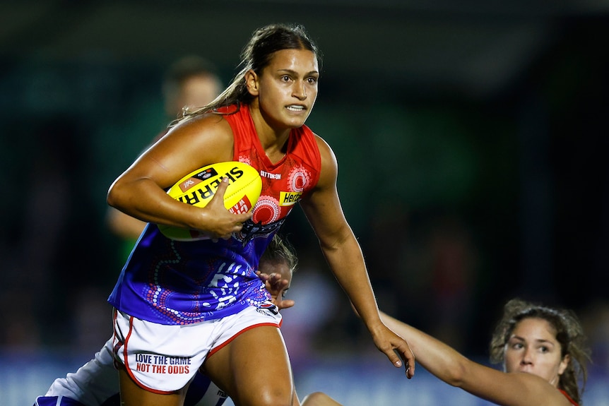 Eliza West runs with the ball during a night game of AFLW.