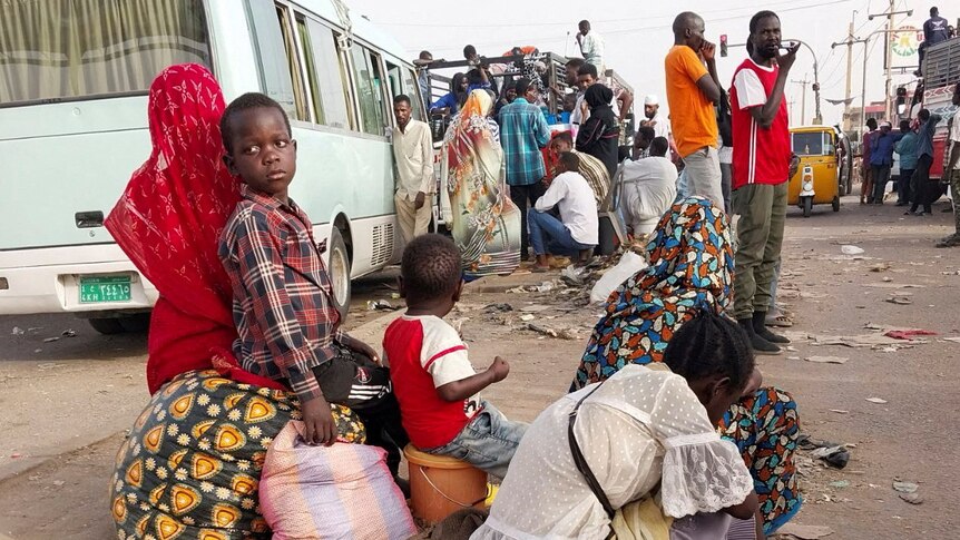 Children sit with their relatives on the side of the road, waiting to get onto vehicles to flee Khartourm.