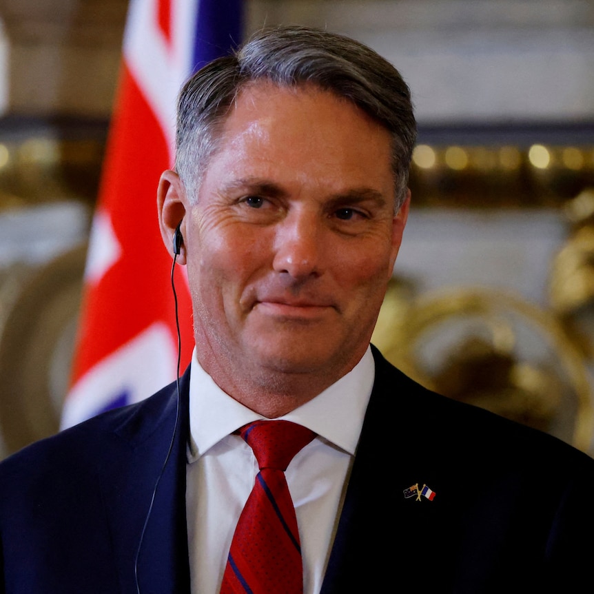 Australia's Defence Minister Richard Marles smiling with earpiece, wearing a red tie and suit jacket.