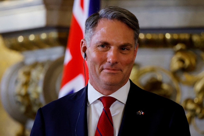 Australia's Defence Minister Richard Marles smiling with earpiece, wearing a red tie and suit jacket.