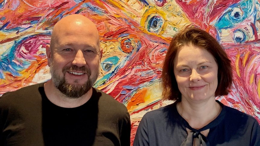 Man and woman standing in front of bright, colourful wall. 