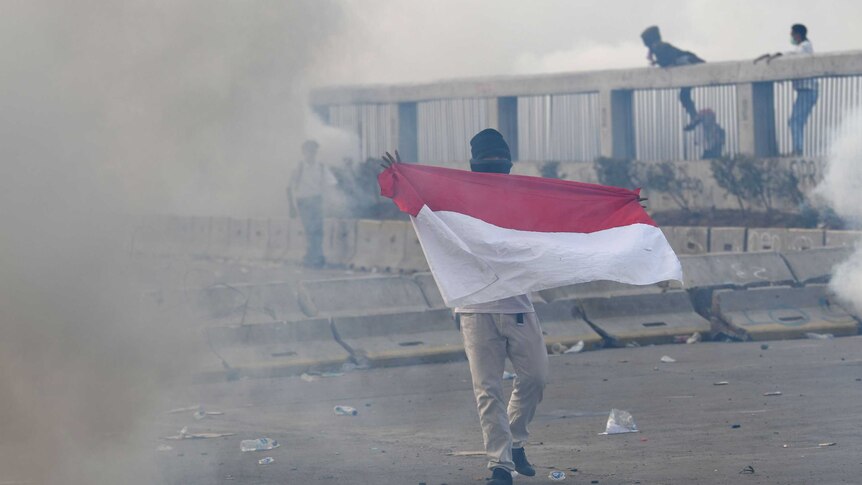 A protester holds Indonesian flag as riot police fire tear gas during a riot.