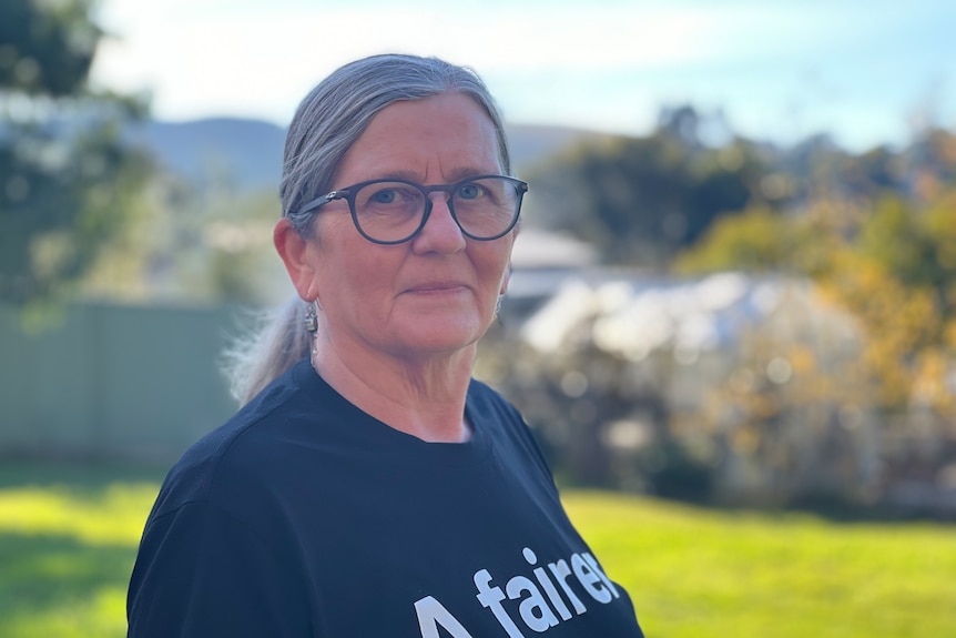 a woman with grey hair and glasses wears a t-shirt that reads a fairer and more just society
