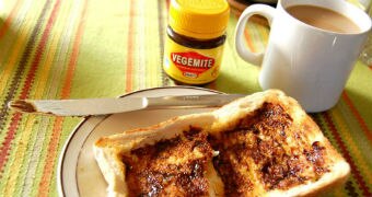 A table setting is seen with a cup of coffee, jar of vegemite and vegemite toast.