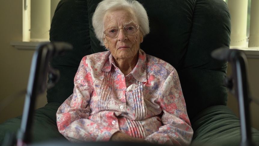 Elderly woman wearing a pink shirt sitting in a chair. 