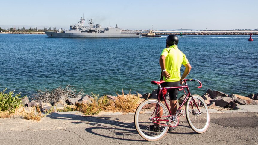 A cyclist watches on as HMNZS Te Kaha arrives in Newcastle.