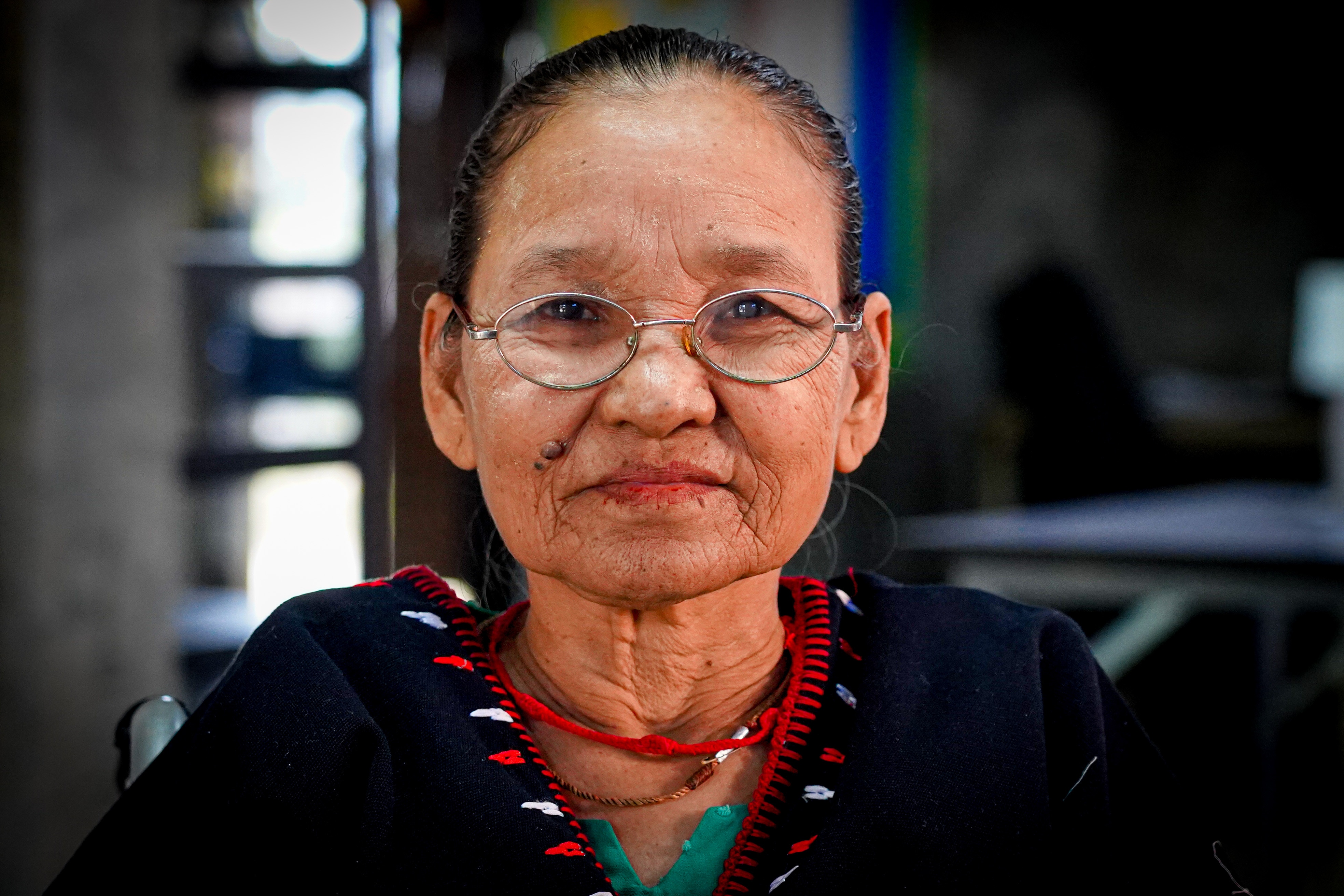 An older Burmese woman in glasses sits in a wheelchair