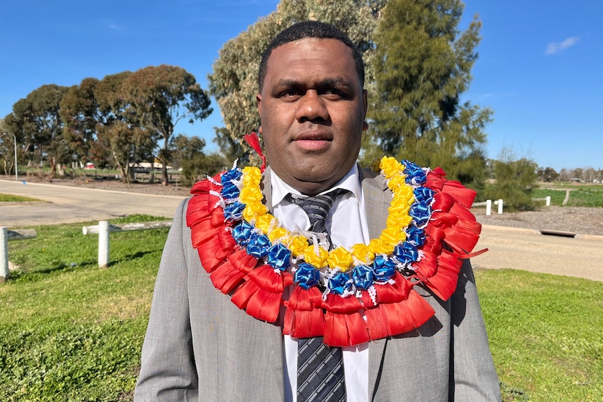 A Fijian man wearing a suit and colorful wreath around his neck.