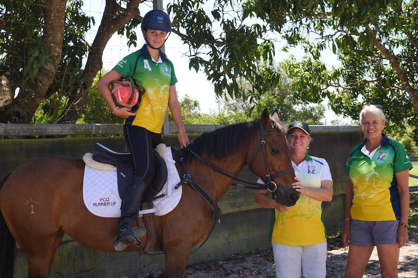 Katie Maund stands upright off the saddle on a horse, her coach Linda Gray and her mother Helen Maund stand beside the horse