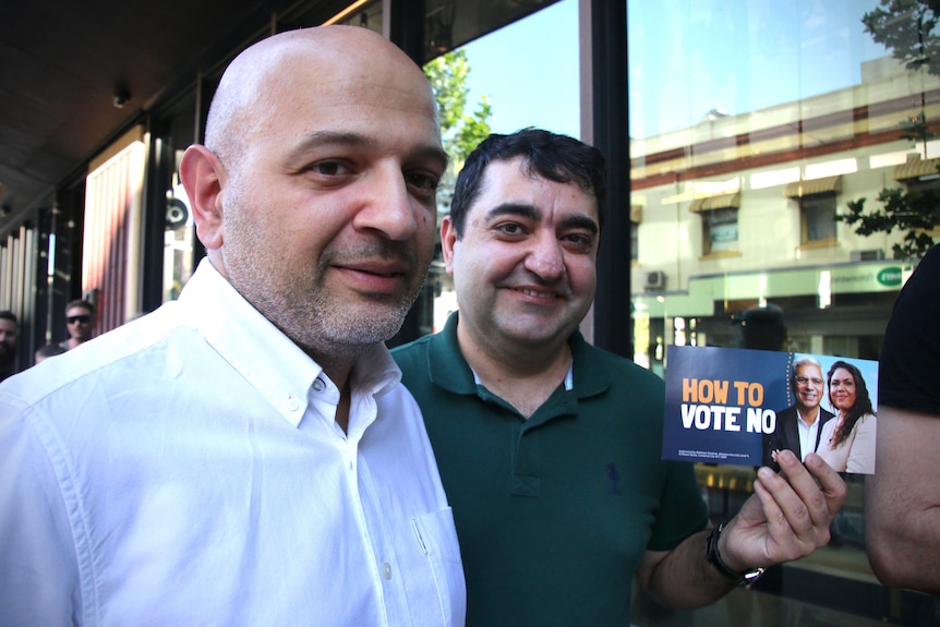 Two men holding a Vote No card