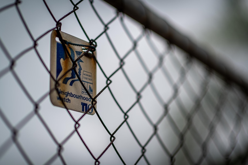 A neighbourhood watch sign is attacked to a fence. The sky looks grey in the background.