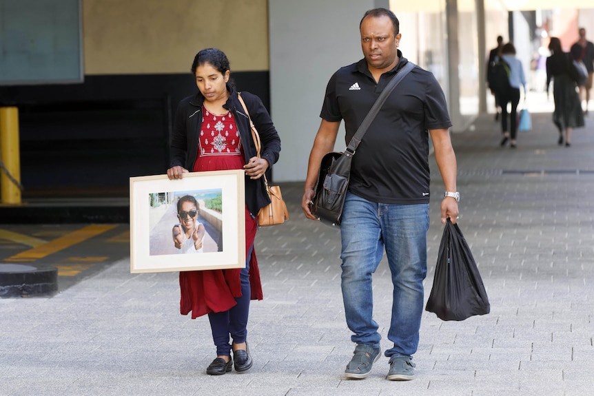 Two people walk down a street carrying a large picture frame